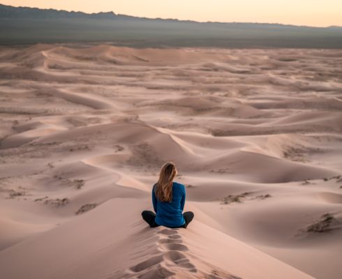Photo of woman sitting cross-legged in sand dunes, grieving grief grieve bereavement loss course death mourning grieving